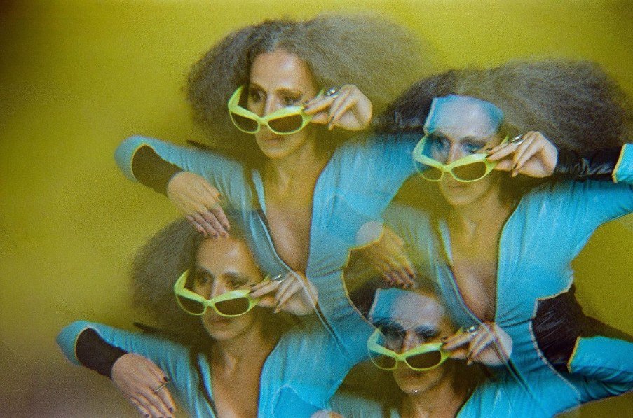 Iara Rennó com óculos de sol verdes em foto de múltipla exposição sobre fundo amarelo