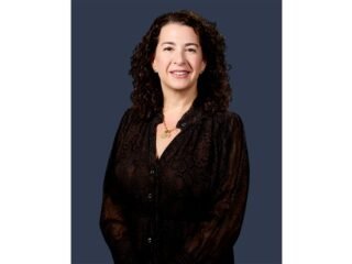 Retrato de Stacie Borteck Dattner, de cabelo cacheado e blusa preta, sobre fundo azul-escuro.