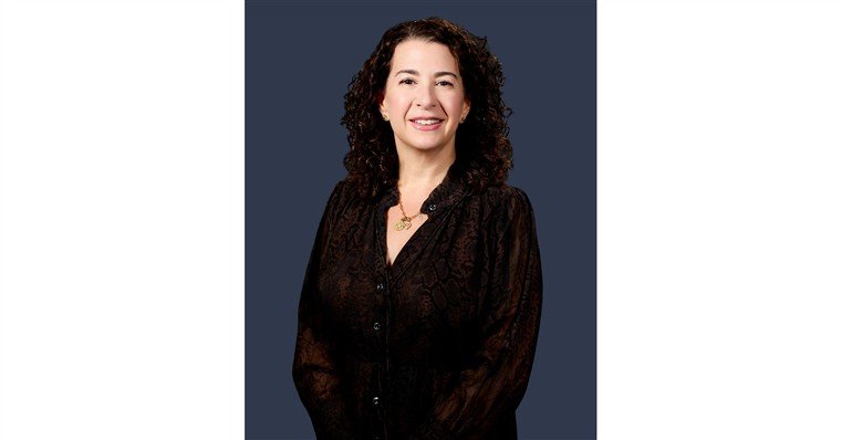 Retrato de Stacie Borteck Dattner, de cabelo cacheado e blusa preta, sobre fundo azul-escuro.