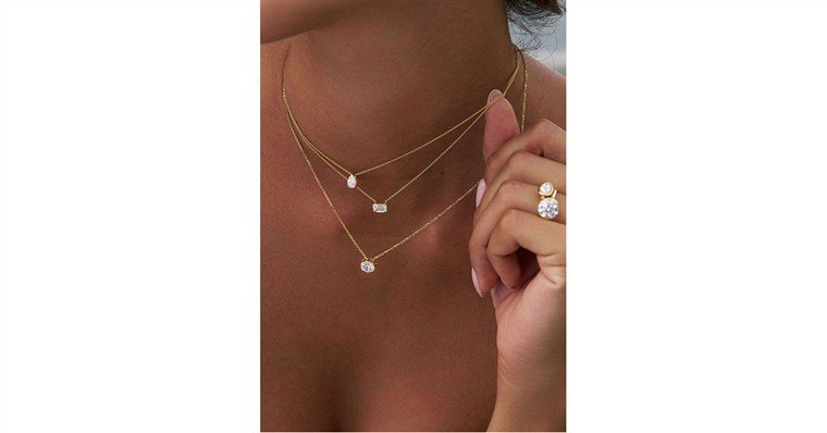 Colares finos de ouro com pingentes de diamante usados em camadas, ao lado de anel com duas pedras.