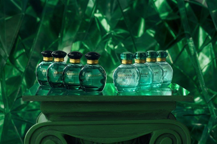 Oito frascos de perfume da coleção Aeonian, em vidro verde, dispostos sobre um pedestal.