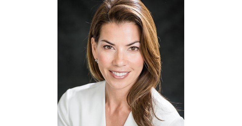 Retrato de Nina Kohler com blazer branco diante de fundo escuro.