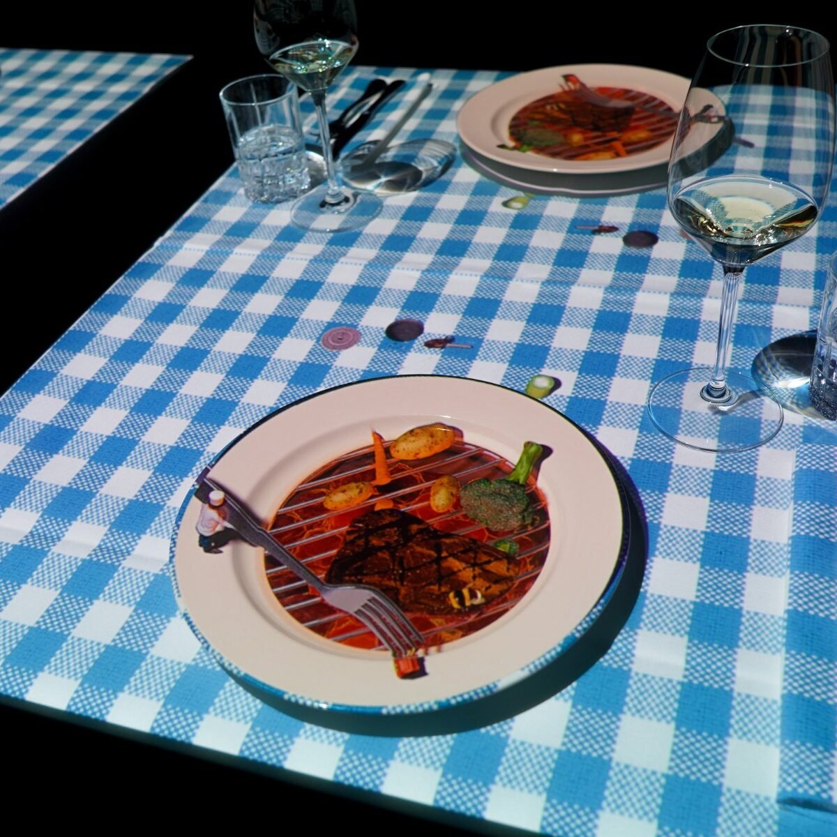 Mesa do Le Petit Chef com toalha xadrez projetada e prato servido, no Hilton Barra Rio de Janeiro