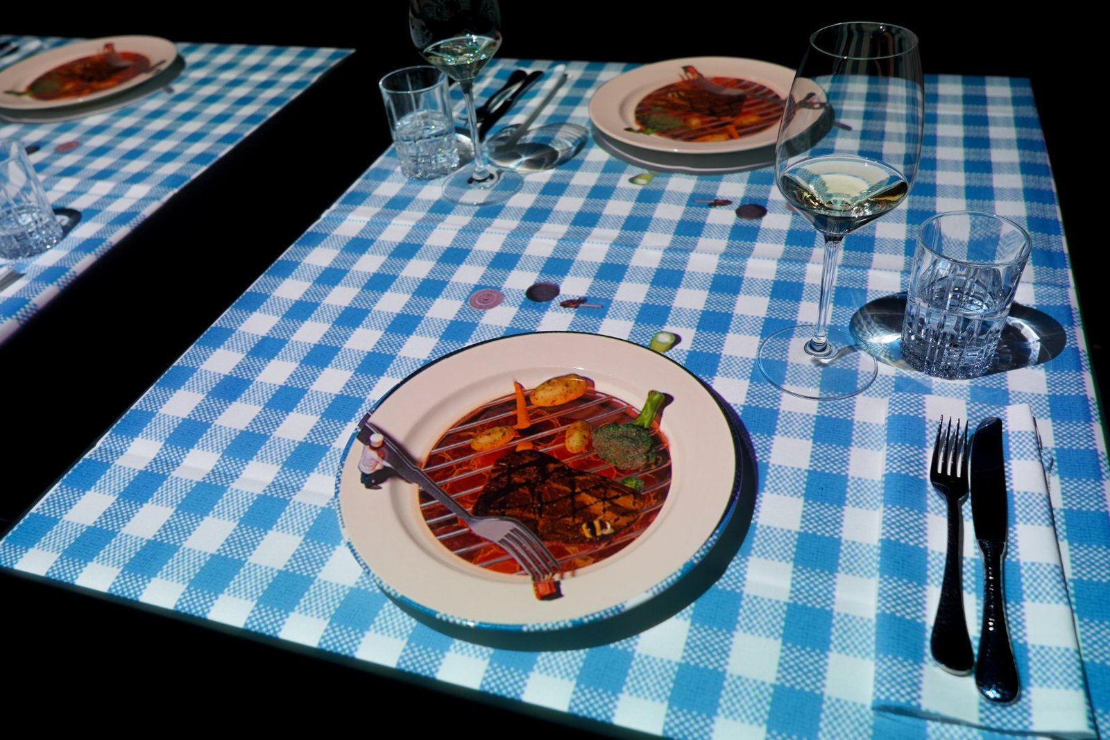Mesa do Le Petit Chef com toalha xadrez projetada e prato servido, no Hilton Barra Rio de Janeiro