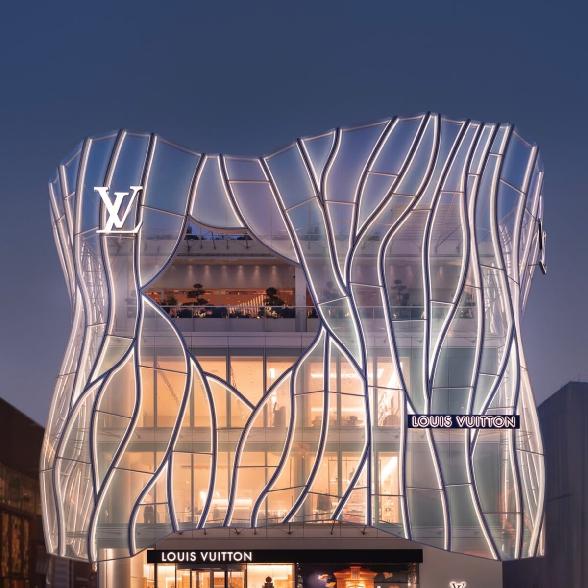 Fachada iluminada da Maison Louis Vuitton Sanlitun, com estrutura de vidro e letreiros da marca.
