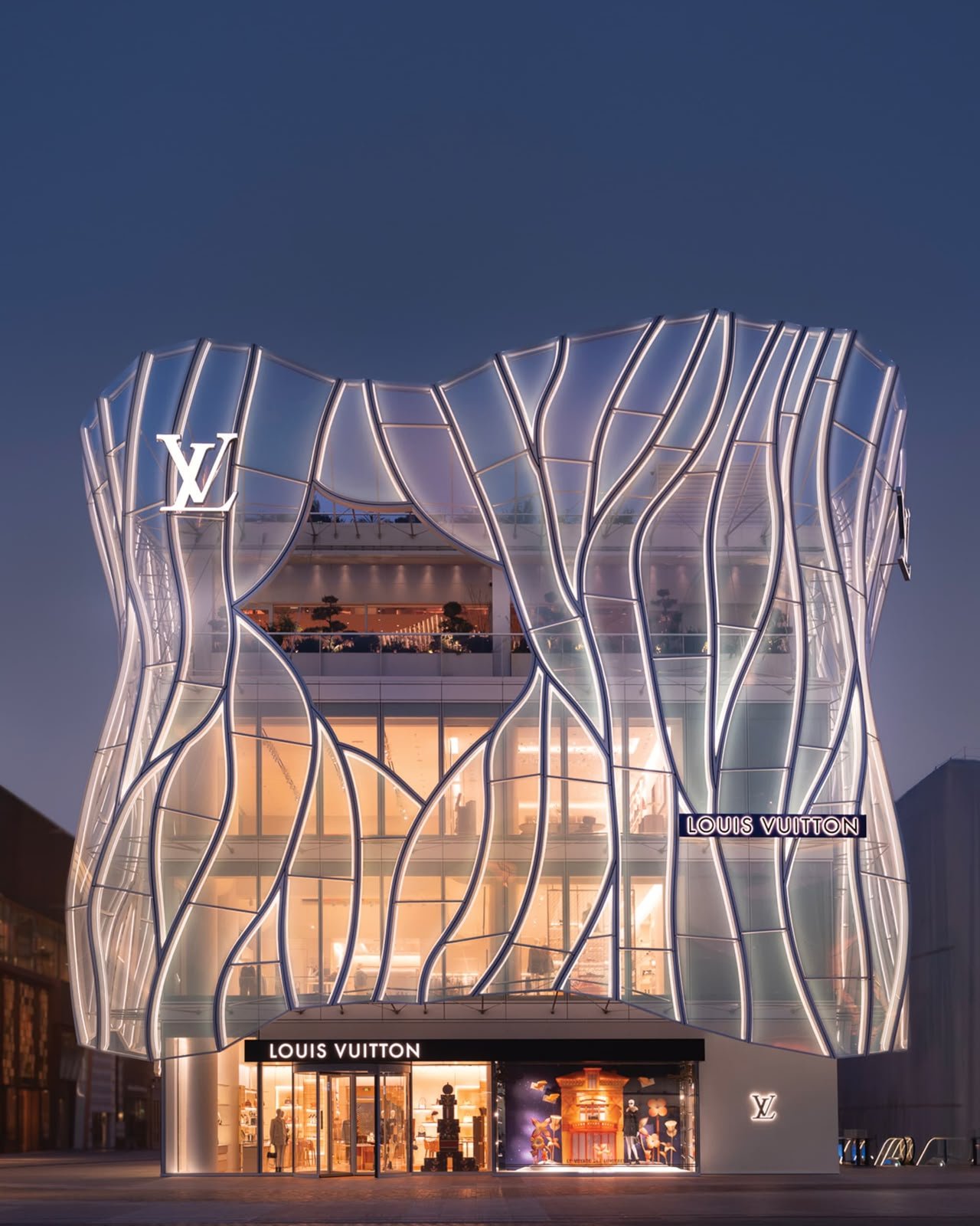 Fachada iluminada da Maison Louis Vuitton Sanlitun, com estrutura de vidro e letreiros da marca.