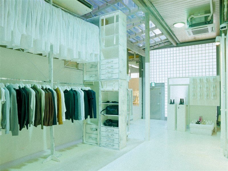 Interior branco da loja Maison Margiela em Tóquio, com araras e estrutura industrial.