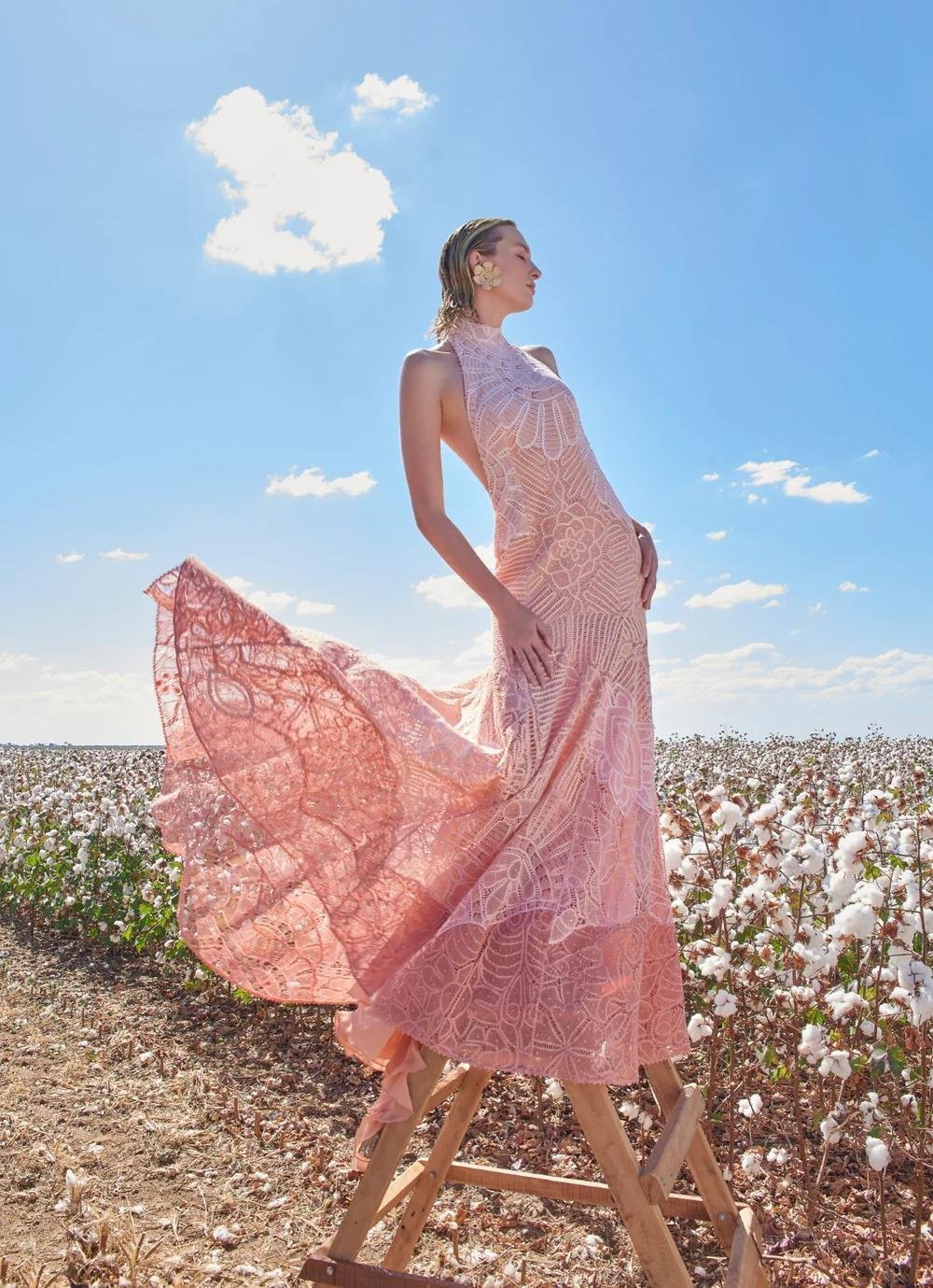 Model in a flowing pink handmade lace dress by Martha Medeiros in a cotton field