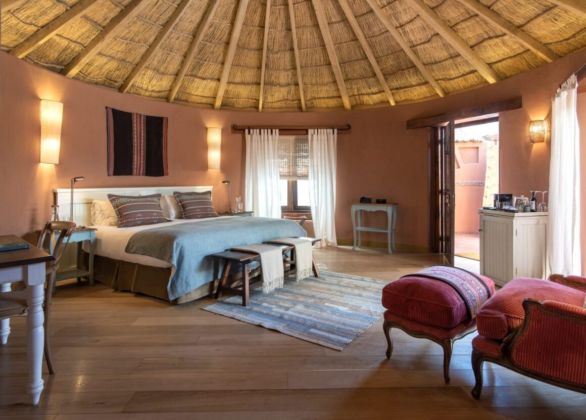 Acomodação do Awasi Atacama com teto de palha, paredes cor de terra e cama com manta azul