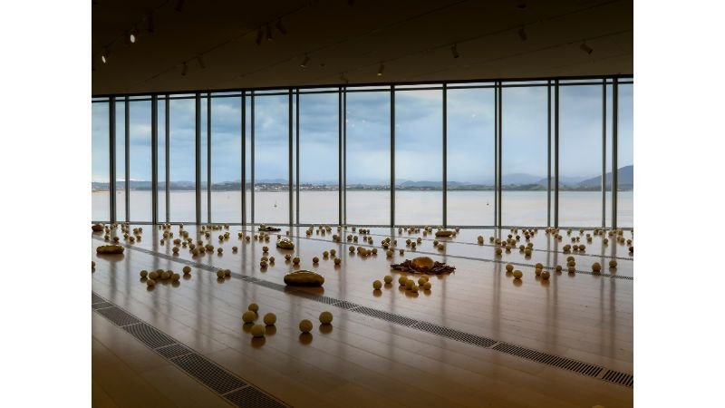 Instalação de Solange Pessoa com elementos orgânicos no piso de sala expositiva com vista para a baía de Santander