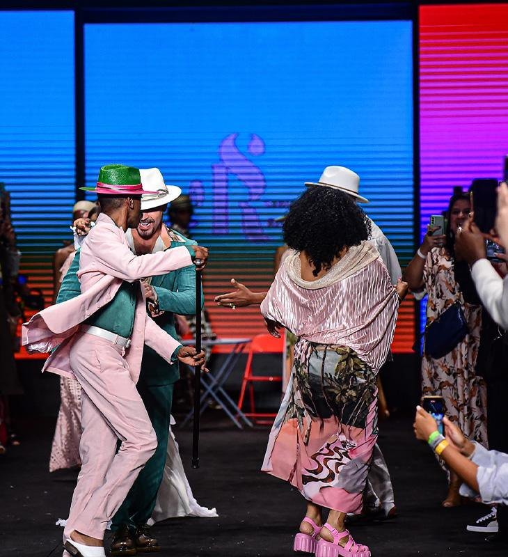 Modelos dançam na passarela com ternos rosa e verde e chapéus, no desfile da Santa Resistência no SPFW N61