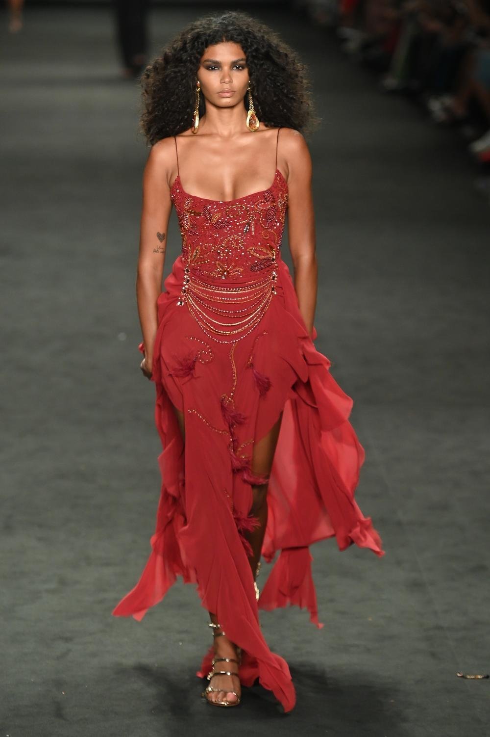 Model in a red beaded gown with gold chains and feathers at the Hisha show, SPFW N61
