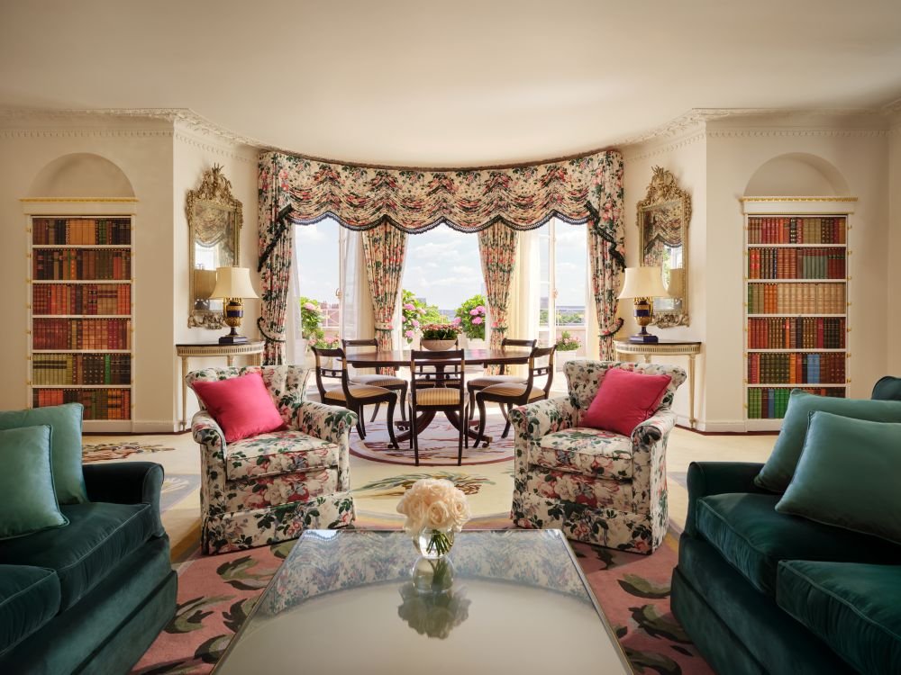 Sala de estar de uma suíte do The Dorchester, em Londres, com estantes de livros e poltronas florais.