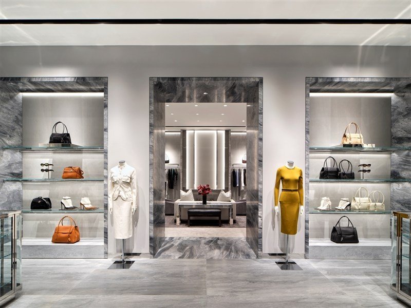 Interior da loja Tom Ford em Costa Mesa, com roupas, bolsas e revestimento de mármore.