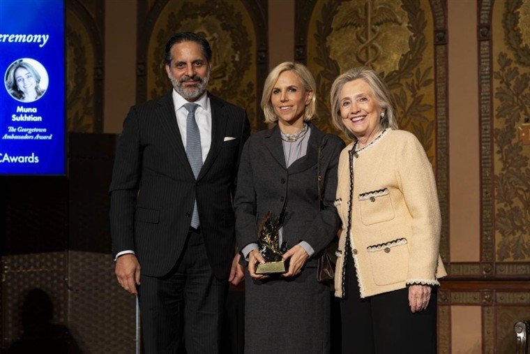 Tory Burch segura o troféu entre Hillary Clinton e um homem de terno, em cerimônia da Universidade Georgetown