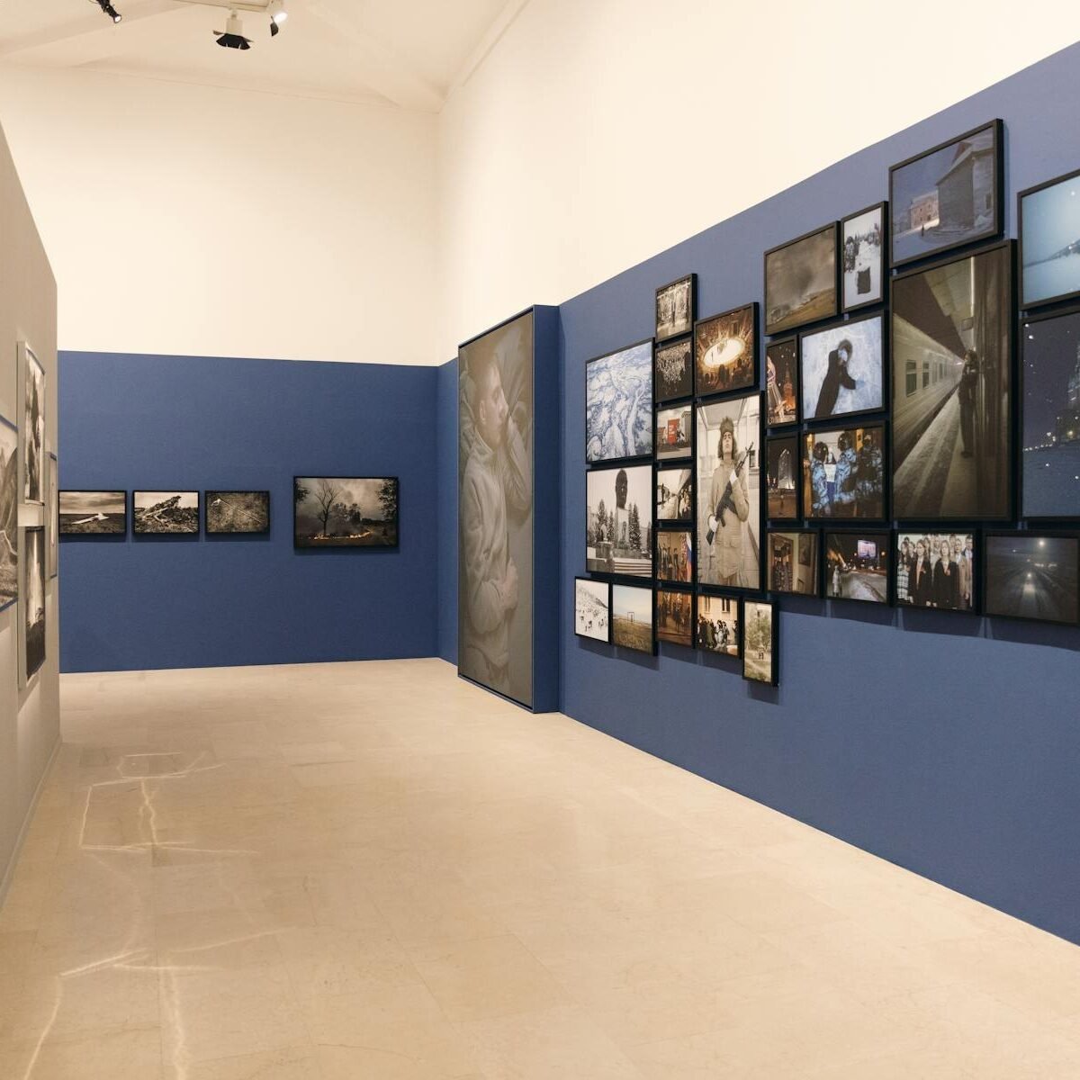Vista da exposição do Photo Grant Deloitte na Triennale Milano, com fotografias emolduradas em paredes azuis e cinza