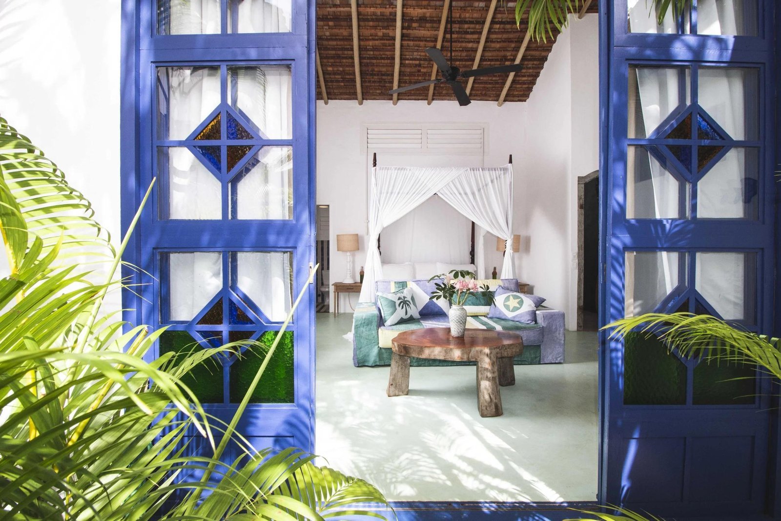 Blue wooden doors opening onto a guest house bedroom with a canopy bed at UXUA Casa Hotel & Spa in Trancoso